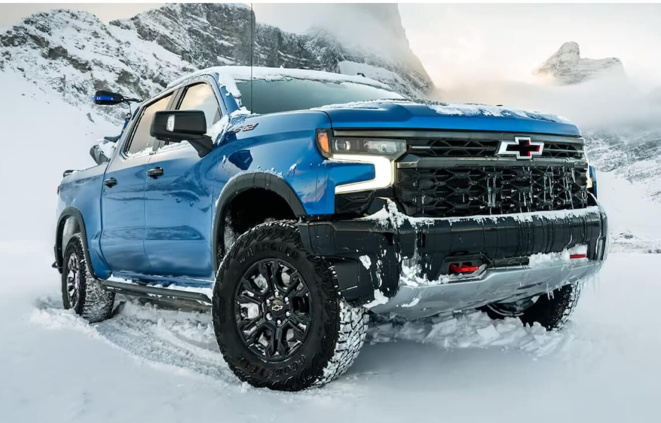 A blue Chevy Silverado drives offroad in packed snow.