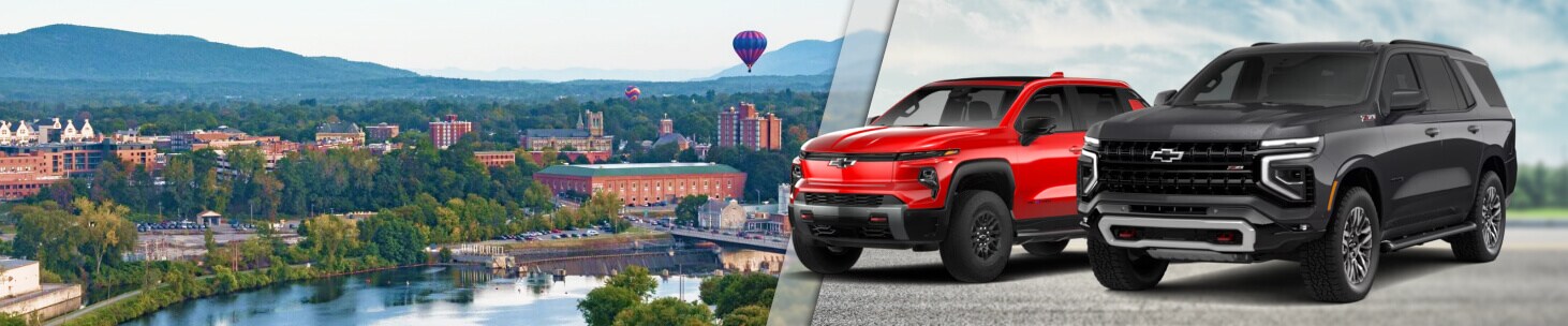 A red Chevy Silverado EV and a black Chevy Tahoe superimposed over an aerial view of Glens Falls NY.