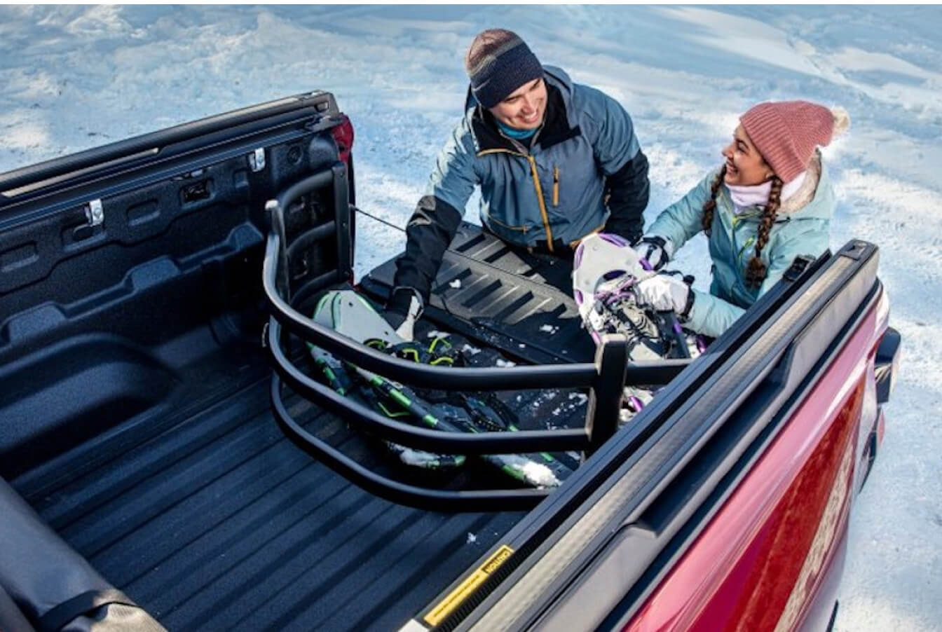Two people unpack snowboarding gear from a Chevy Silverado truck bed.