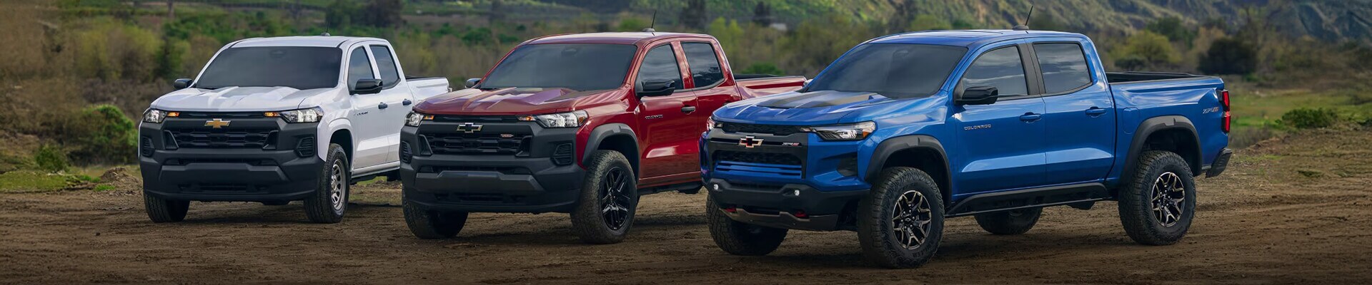 Three Chevrolet Colorado Trucks in white, red, and blue parked in front of mountainous terrain