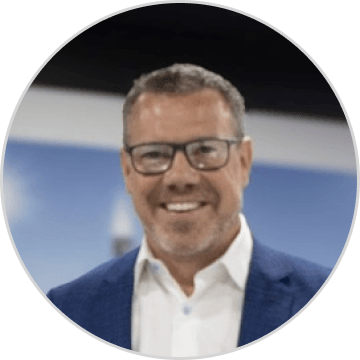 Headshot portrait of Scott Bell wearing a blue jacket and glasses against a blurred background.
