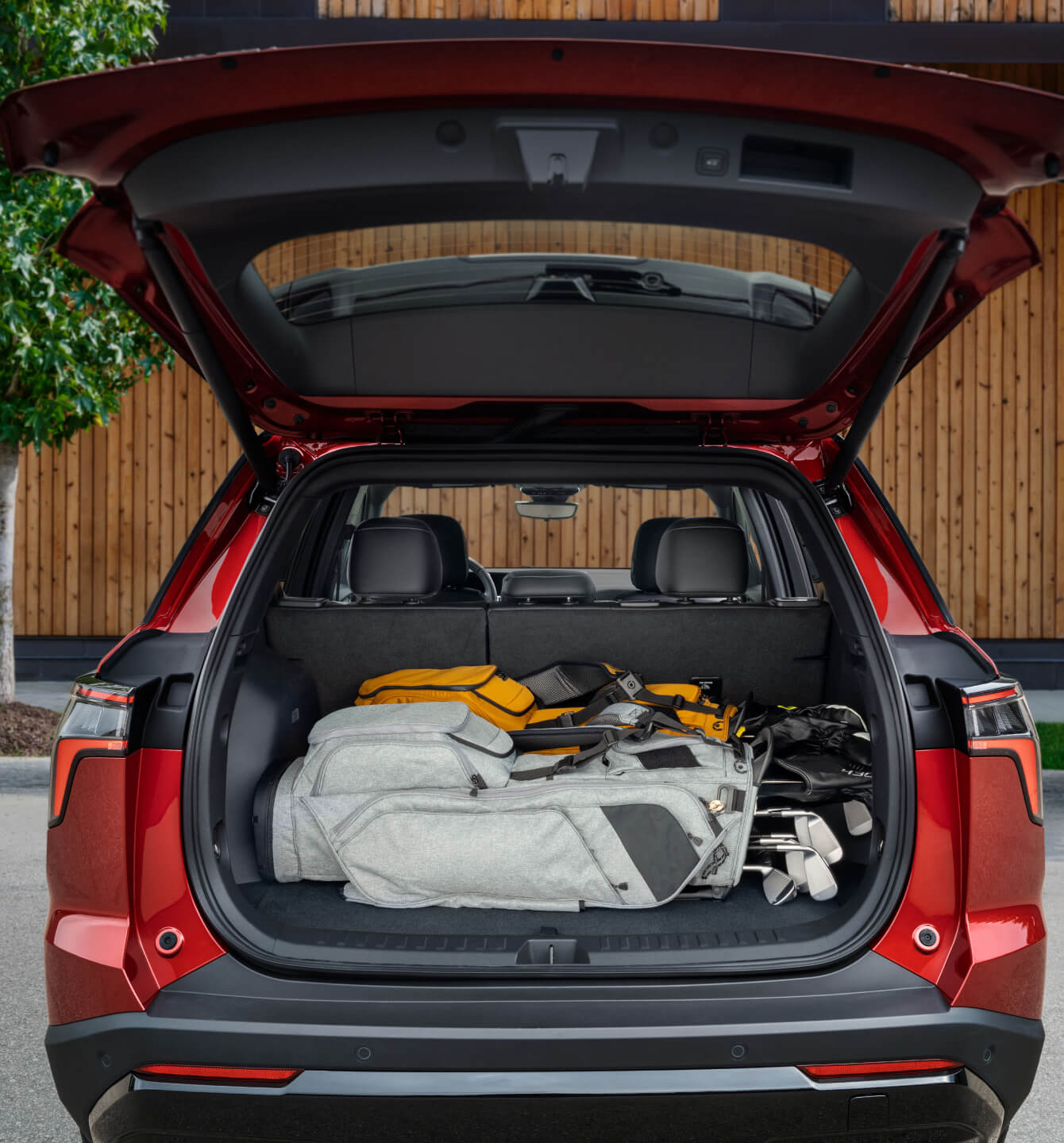 Rear view of open trunk red Chevrolet Equinox filled with golf bags in front of wooden building.