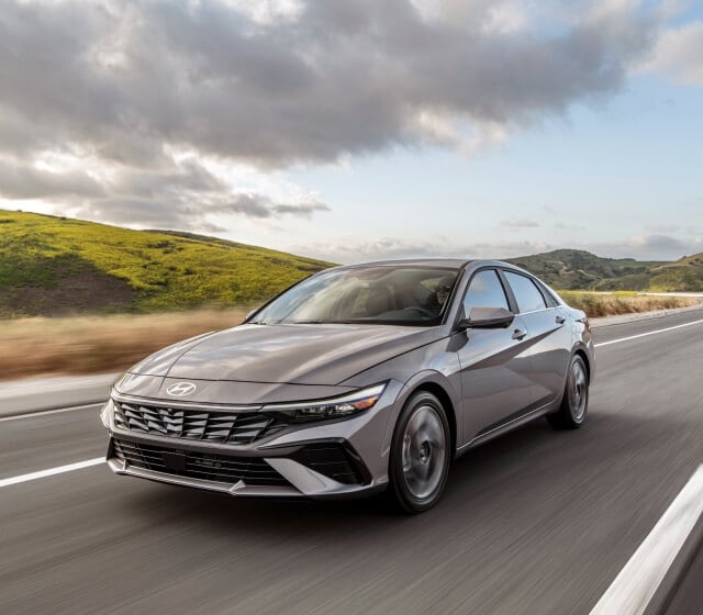 A new 2025 Hyundai Elantra driving on the highway in front of a hilly landscape
