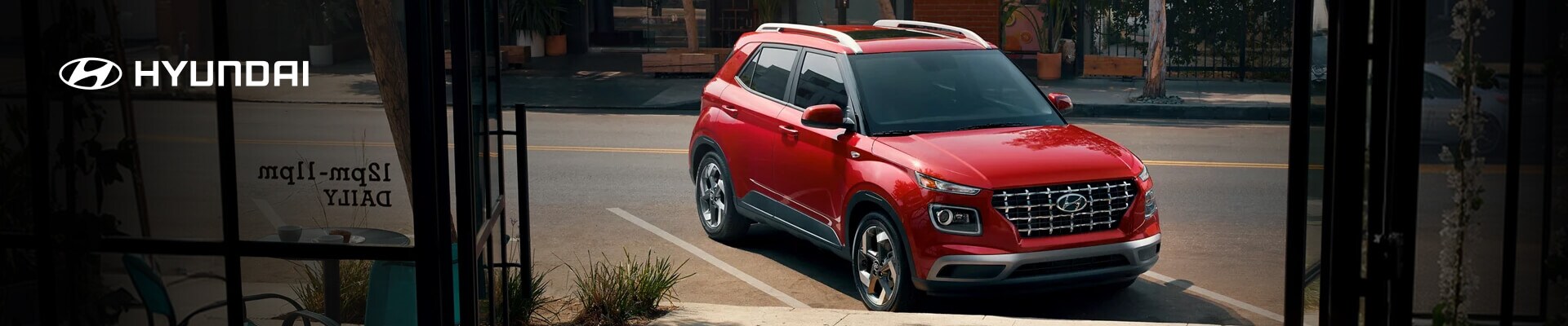 2026 Hyundai Venue in Ultimate Red, front three-quarter view parked outside a city shop.