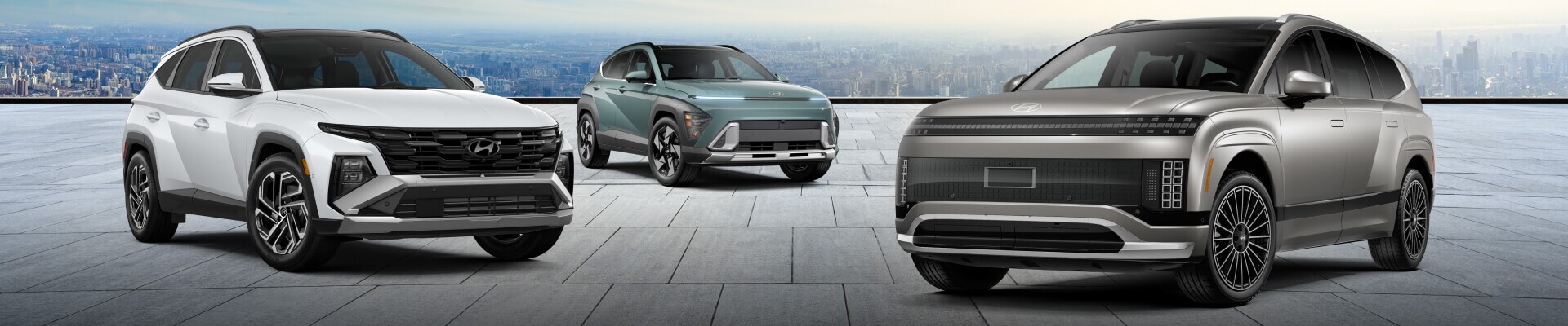 Three Hyundai SUVs parked on a stone terrace with a city skyline background: a white Tucson, a sage green Kona, and a silver INOIQ 9