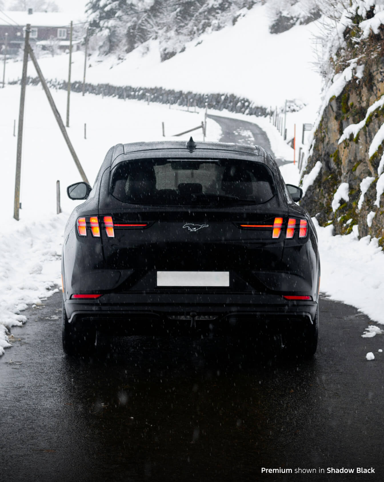 Rearview of a new Mustang Mach E Premium in Shadow Black driving in snowy conditions