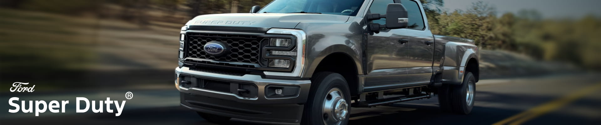 A gray Ford Super Duty pickup truck driving on a paved road, shown from a front three-quarter angle with a motion-blurred background.