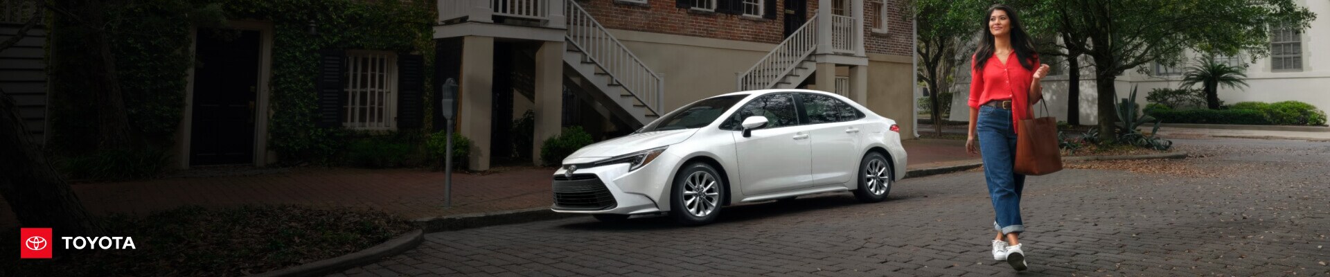 Wind Chill Pearl Toyota Corolla Hybrid LE parked on a historic brick street as a woman is walking past.