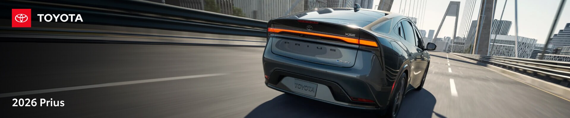 2026 Toyota Prius Plug-in Hybrid XSE in Guardian Gray, rear three-quarter view driving across a city bridge.