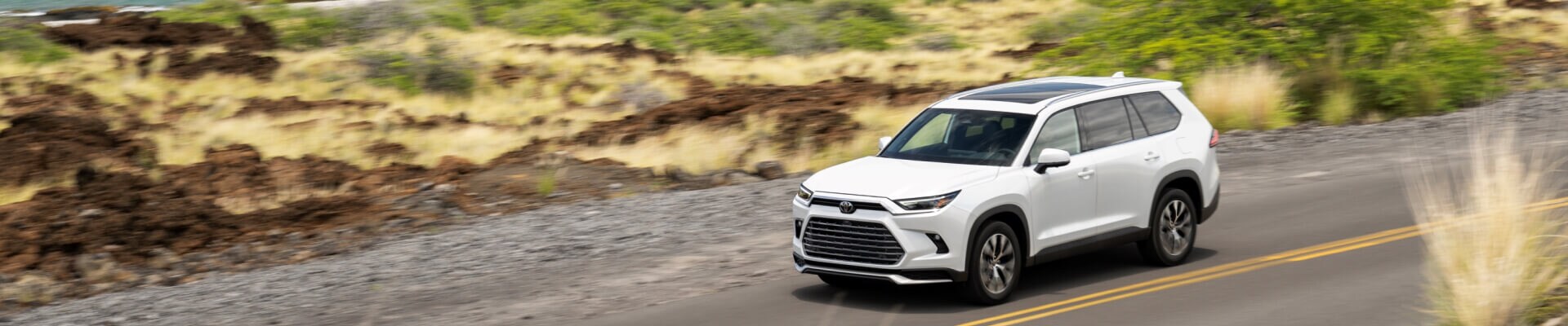 High angle view of 2026 Toyota Grand Highlander in white driving on a highway coast.