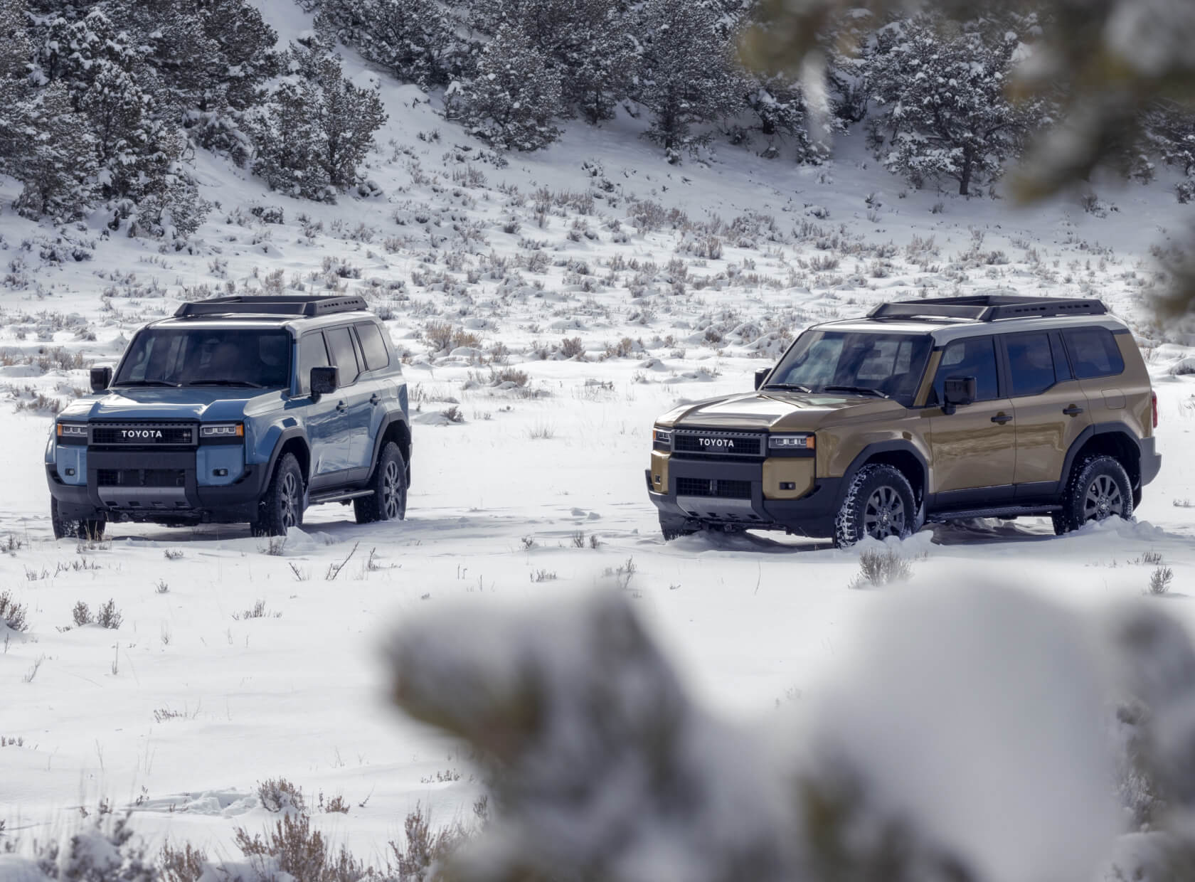 Toyota Land Cruiser First Edition in Heritage Blue and Trail Dust with roof racks on snowy terrain.