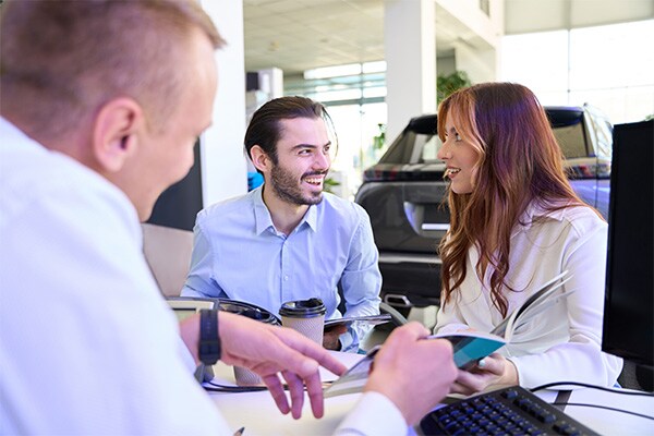 Young couple sitting down at a desk with auto sales consultant