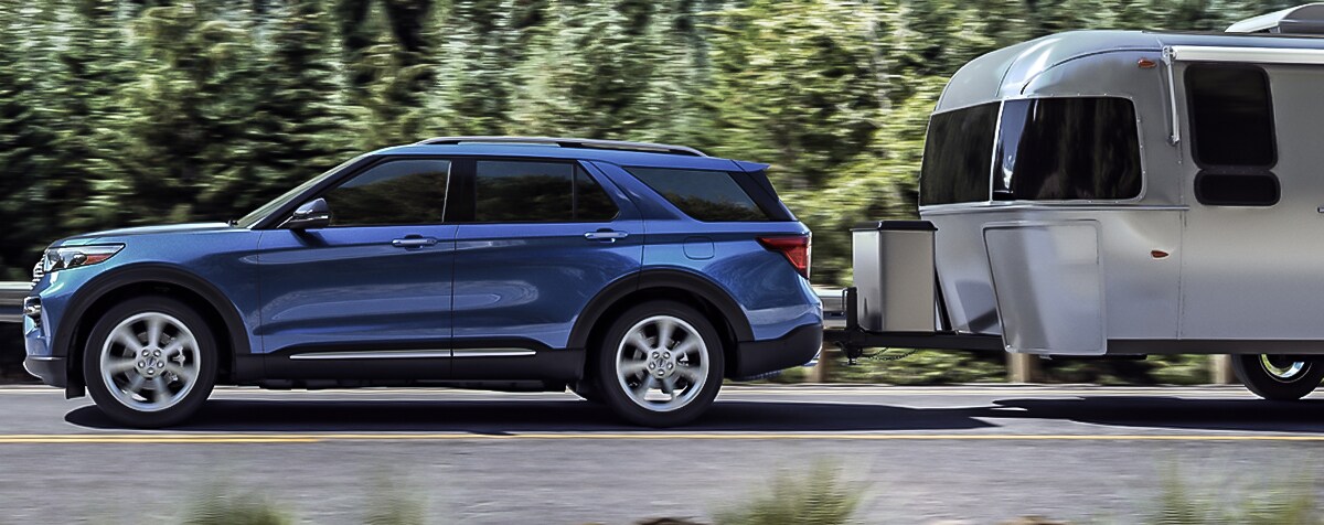 2020 blue Ford Explorer driving through a wooded area towing a trailer