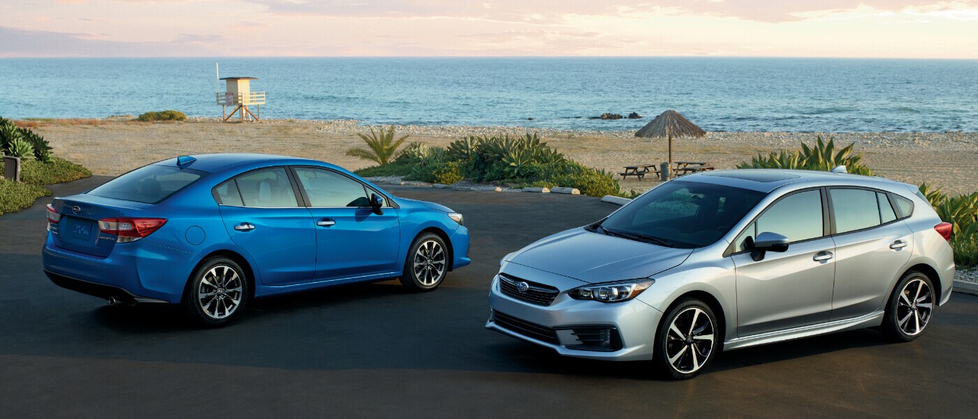 2020 Subaru Impreza in blue and hatchback in gray parked in parking lot with beach in the background
