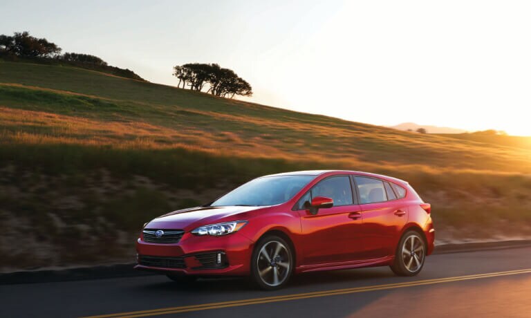 2020 Subaru Impreza in red driving on highway with hilly plans along it