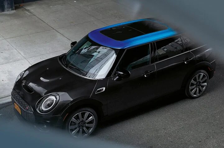 Clubman Roof Aesthetics - 7.webp View from above of a black MINI Clubman that is parked on a city street.