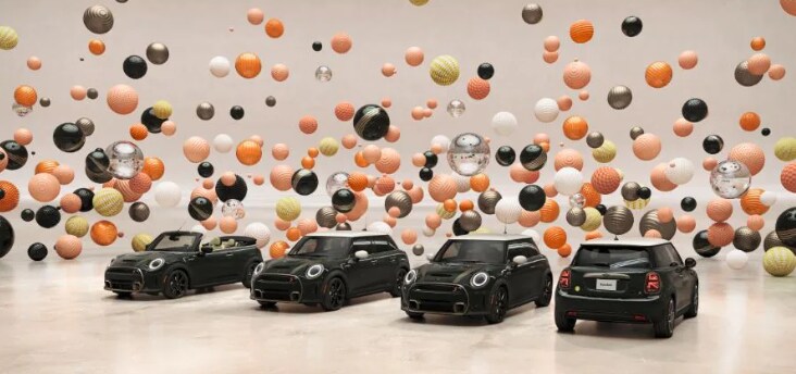 Overhead three quarter view of four MINI ResoluteEditions, a 2 Door, 4 Door, Convertible, and Electric, in a CGIworld filled with floating, multi color and multi texture balls.