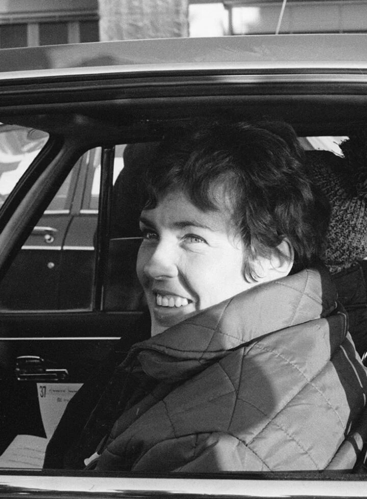 3.jpeg Pat Moss sitting in the driver's seat of a car, in a black and white photo, smiling and glancing out the window.