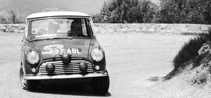 4.jpeg MINI vehicle rounding the corner of a bend, in a black and white photo, with trees in the background.