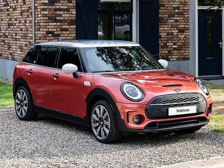 11.jpg Three-quarters front view of a MINI Clubman Multitone Edition in Coral Red parked in front of a brown brick building.