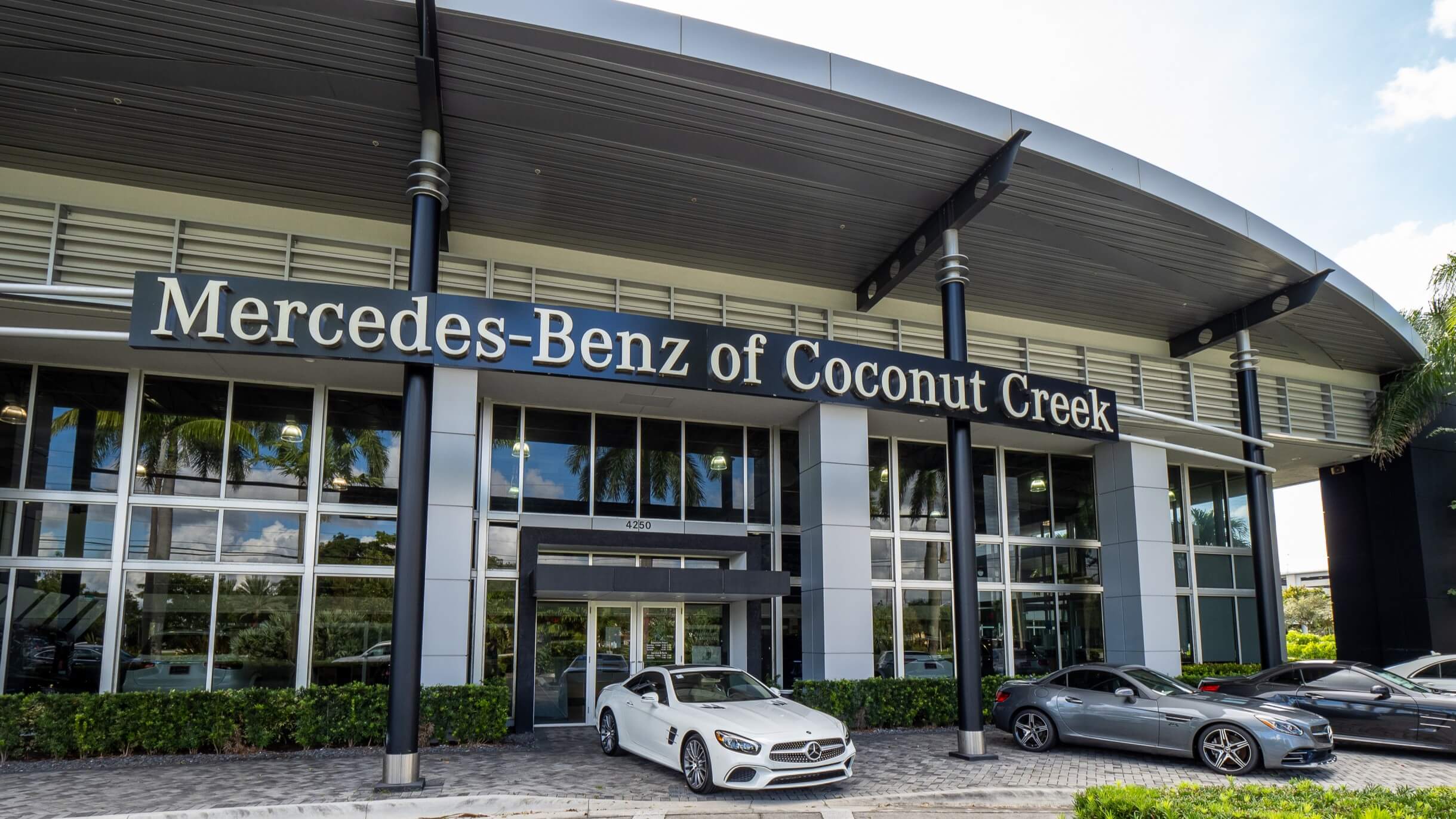 Picture of the front of Mercedes-Benz of Coconut Creek dealership with sedans parked in front