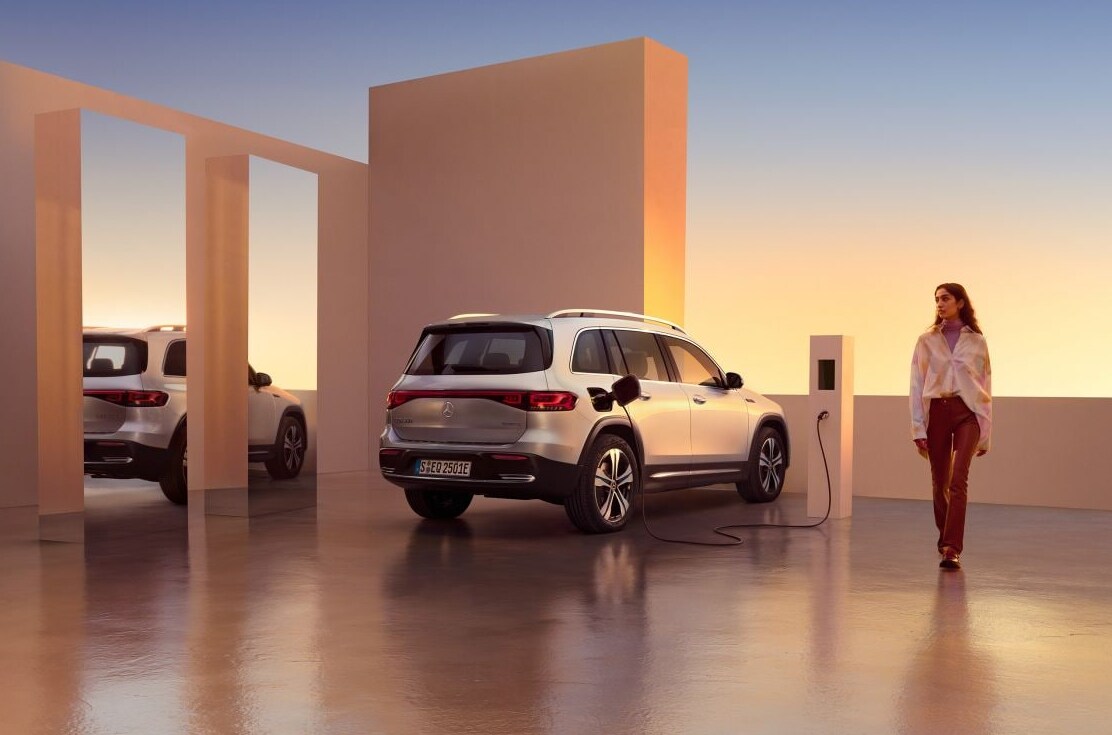 2022-Mercedes-Benz-EQB-1.PNG A white 2022 Mercedes Benz EQB sits parked at a charging station while a woman walks away