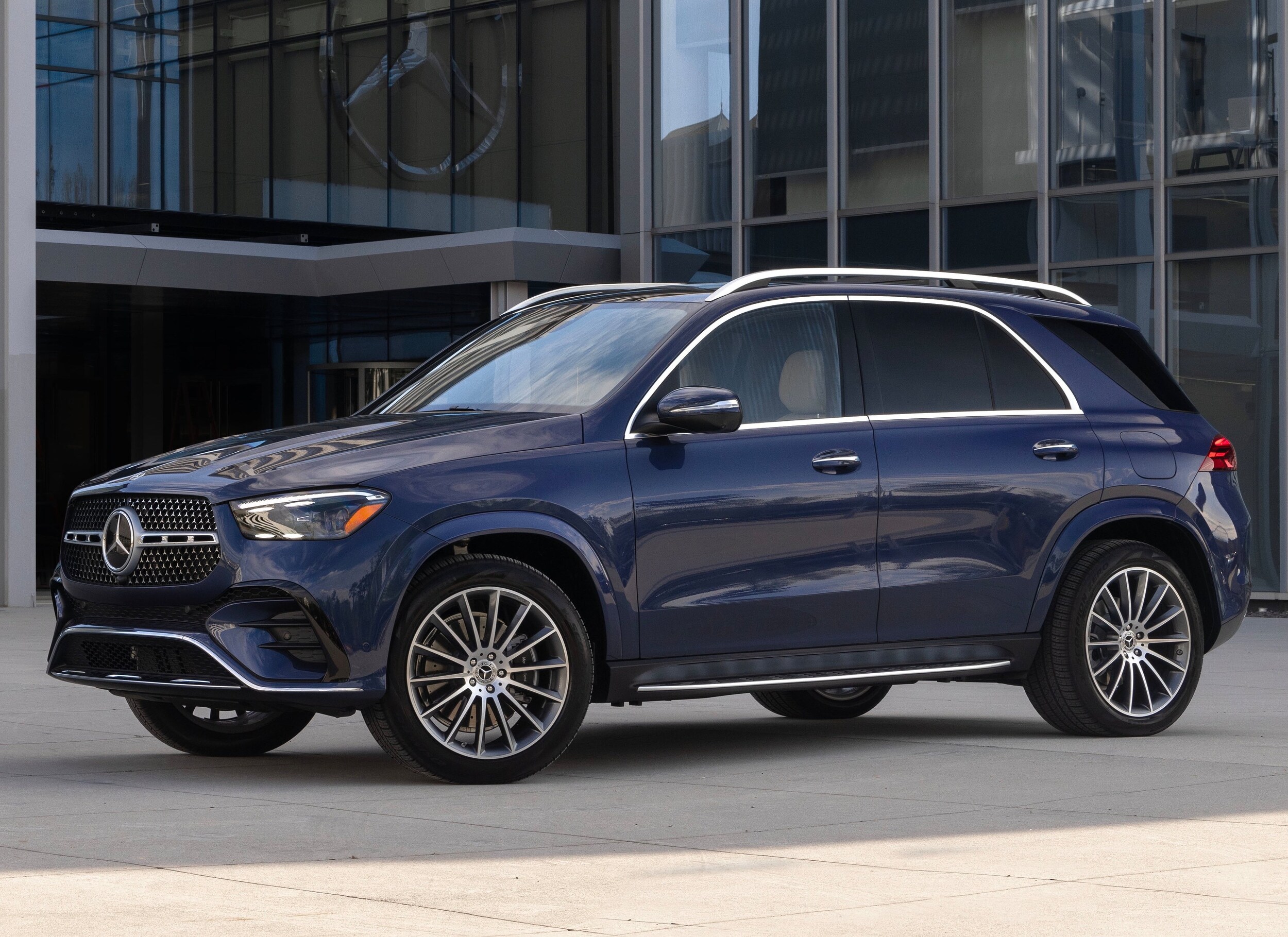 Mercedes-Benz-GLE-2024-wallpaper.jpg A blue Mercedes-Benz parked in front of a corporate office.