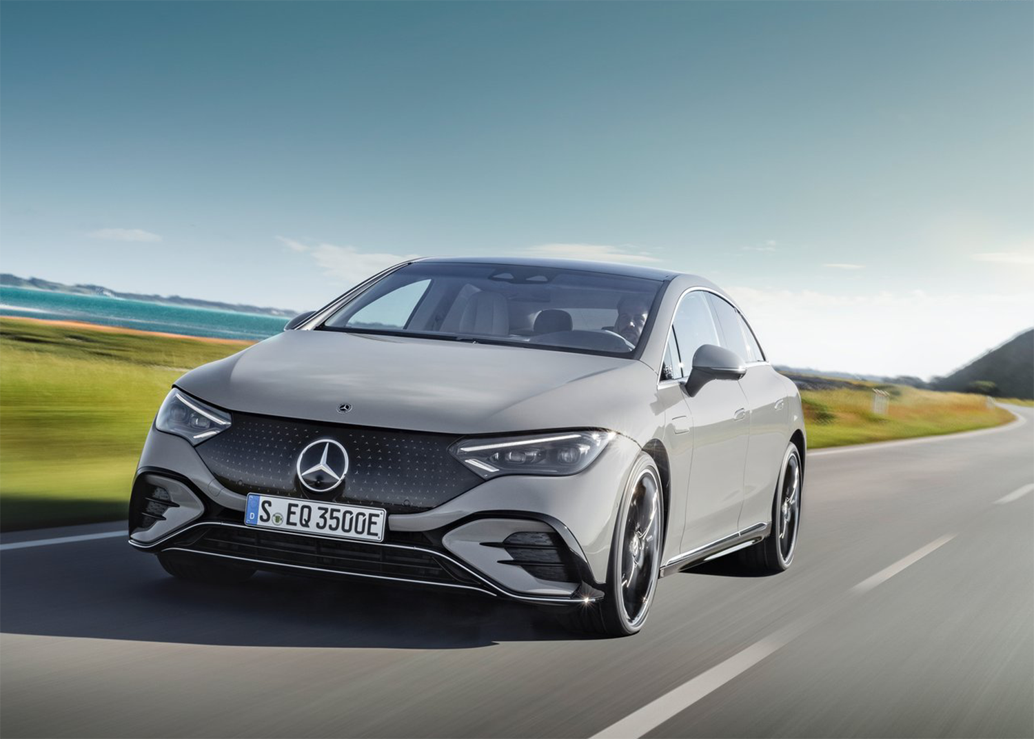 MB%20EQE%202024%205.30.png A Mercedes-Benz EQE driving down a road surrounded by a grassy field.
