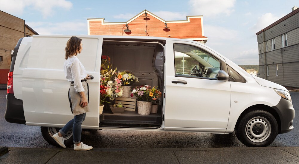 A woman opening the sliding door of a white 2024 Mercedes-Benz Metris cargo van with flowers inside.