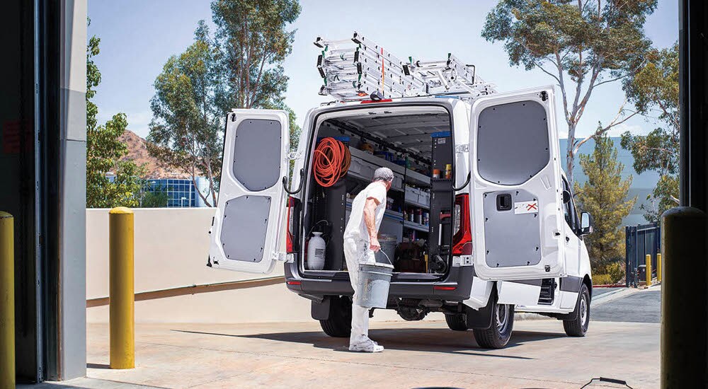An electrician reaching into the open cargo area of a white 2024 Mercedes-Benz Sprinter 2500.