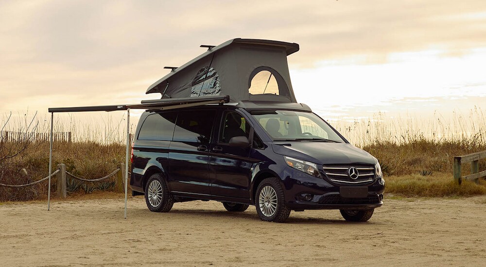 A black 2024 Mercedes-Benz Metris passenger van with a camper upfit parked at the beach.
