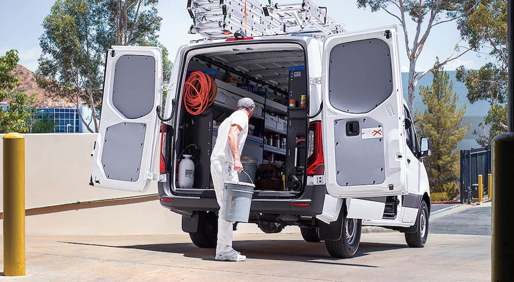 A man loading gear into the open back of a white 2025 Mercedes-Benz Sprinter 2500 Cargo Van.