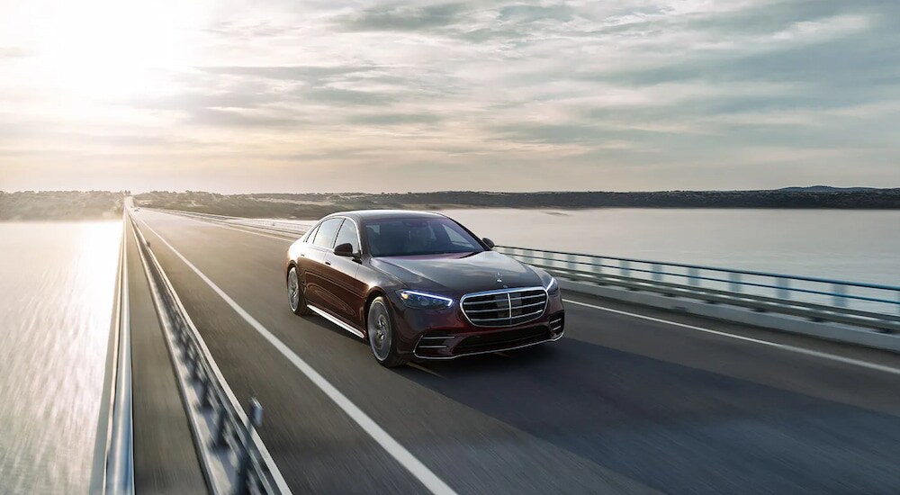 A dark maroon 2024 Mercedes-Benz S 580 AMG Line driving on a bridge.