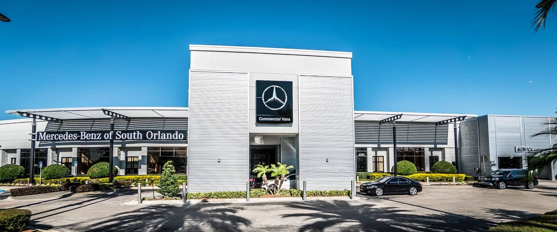 The Mercedes-Benz of South Orlando showroom, with the Mercedes-Benz star sign above its entrance, seen from across the palm-lined front driveway
