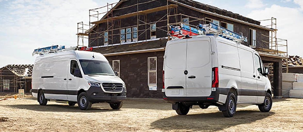 Two white Sprinter Cargo Vans with roof ladder racks parked outside a house under construction