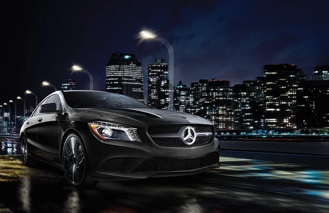 A black Mercedes-Benz CLA on a city street at night with the skyline lit behind it