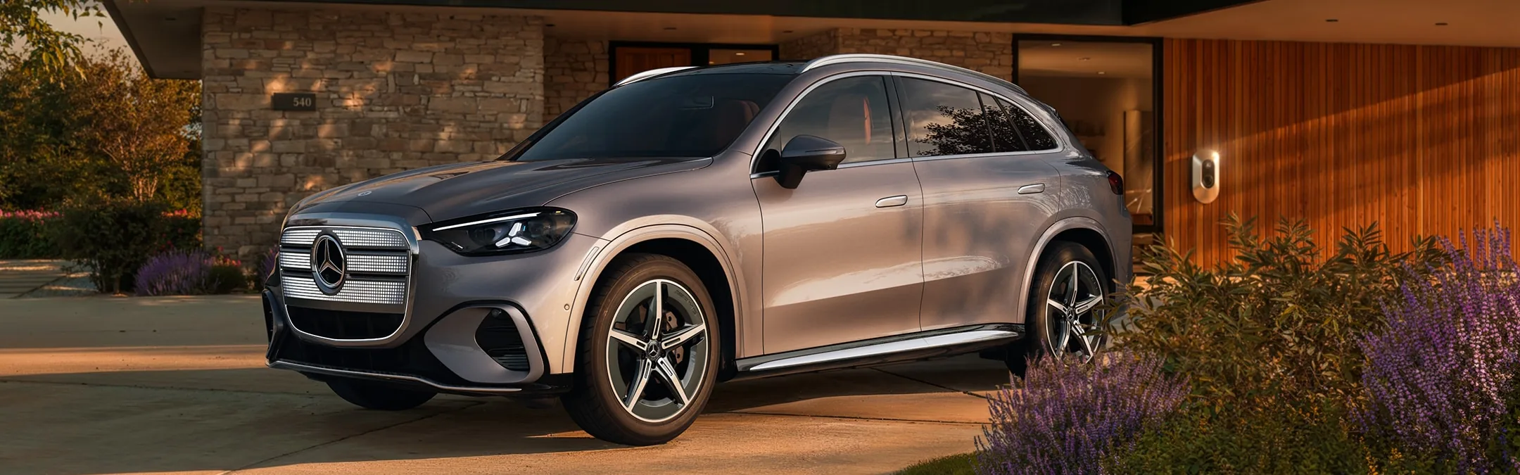 Silver 2027 Mercedes-Benz GLC Electric SUV in a home driveway at sunset