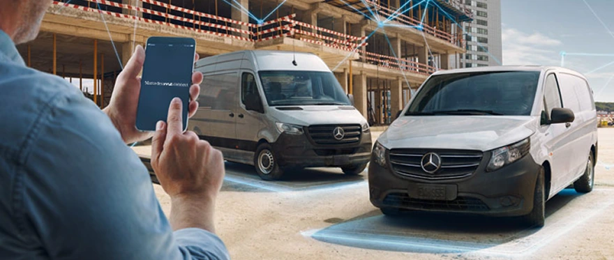 Worker holding a phone beside two Mercedes-Benz vans at a construction site, each van ringed by a blue connectivity glow