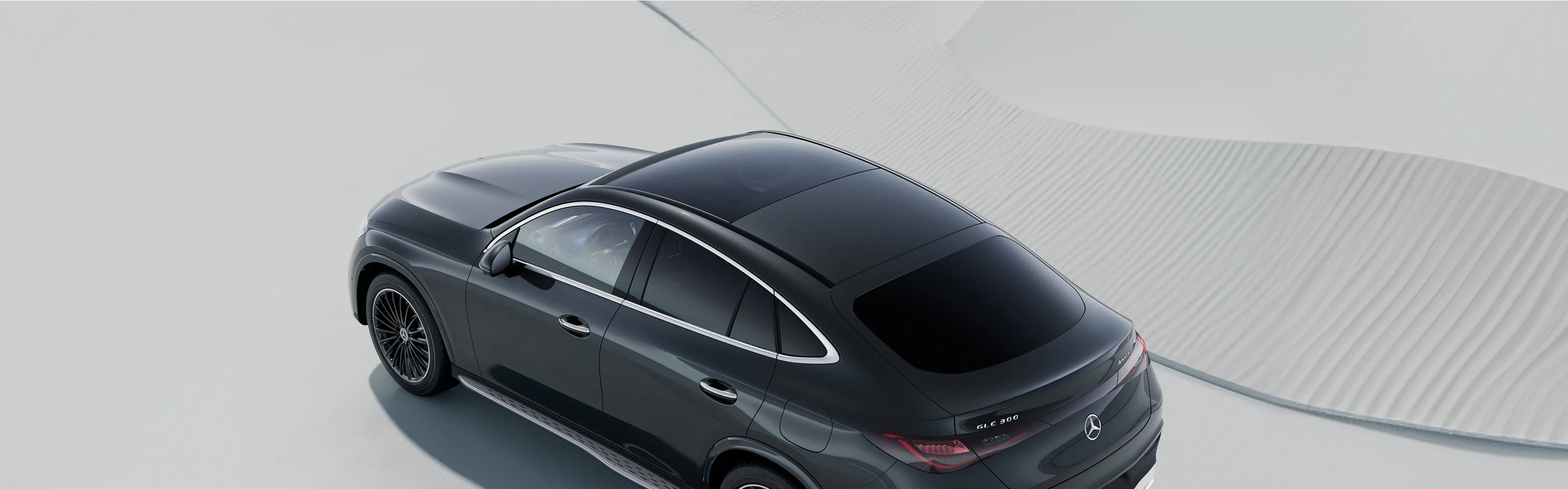 Overhead view of a dark grey 2027 Mercedes-Benz GLC Coupe on a pale sculpted surface