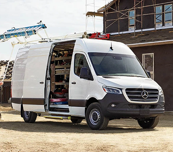 White Sprinter Cargo Van with a roof ladder rack and its side door open at a building site