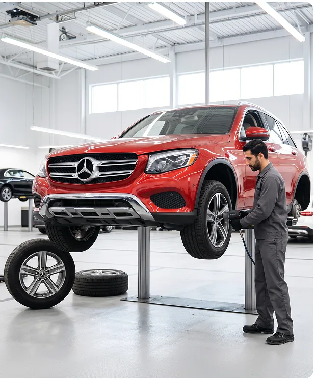 Technician using an impact wrench on the front wheel of a red Mercedes-Benz GLC raised on a service lift, with removed wheels on the floor beside it