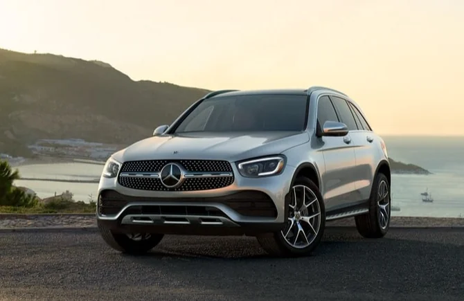 A silver Mercedes-Benz GLC parked on a coastal road at sunset above the sea