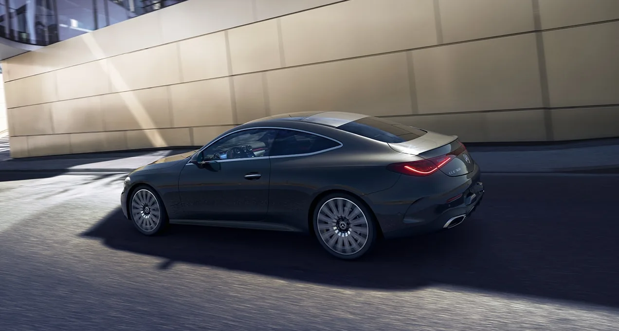 Dark grey CLE Coupe driving past a sunlit concrete wall