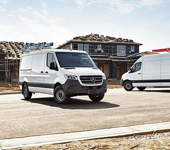 Two white Sprinter Cargo Vans parked on the street of a housing development under construction