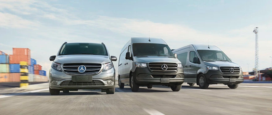 Three white Mercedes-Benz Sprinter vans parked side by side on a dockside lot