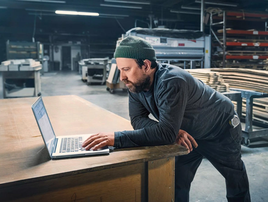 Fleet manager working on a laptop in a warehouse beside a parked Mercedes-Benz van