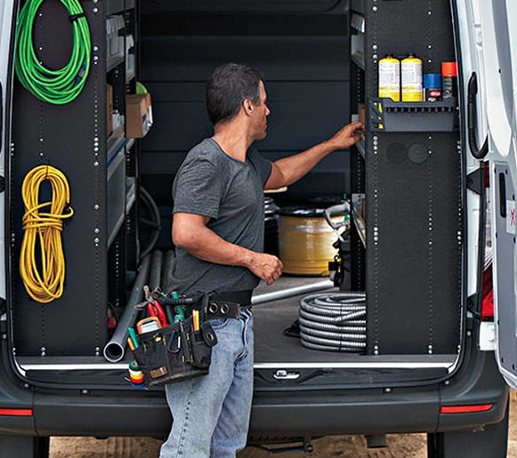 Tradesperson at the open rear doors of a Sprinter fitted with shelving, hose reels and tool storage
