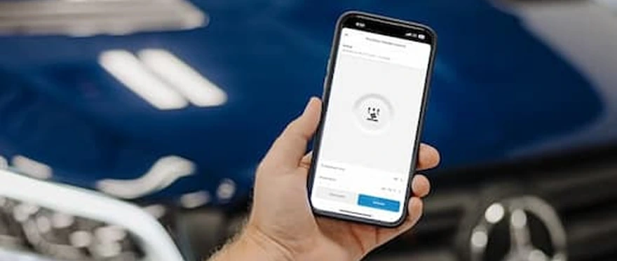 Hand holding a phone with the app's pre-conditioning screen open in front of a blue Mercedes-Benz van