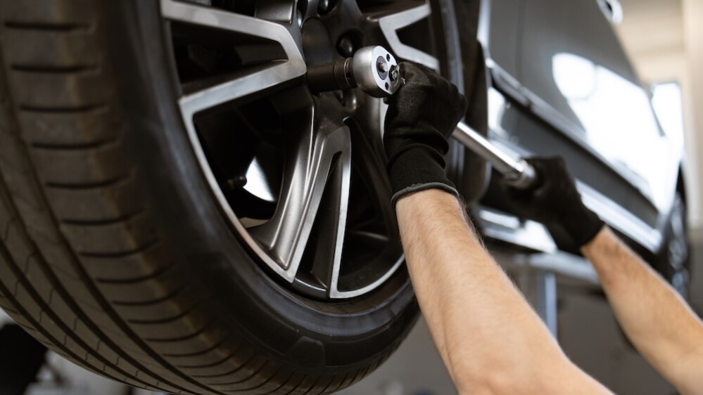 The arms of a white person in black gloves adjusting a vehicle's tire with a large wrench