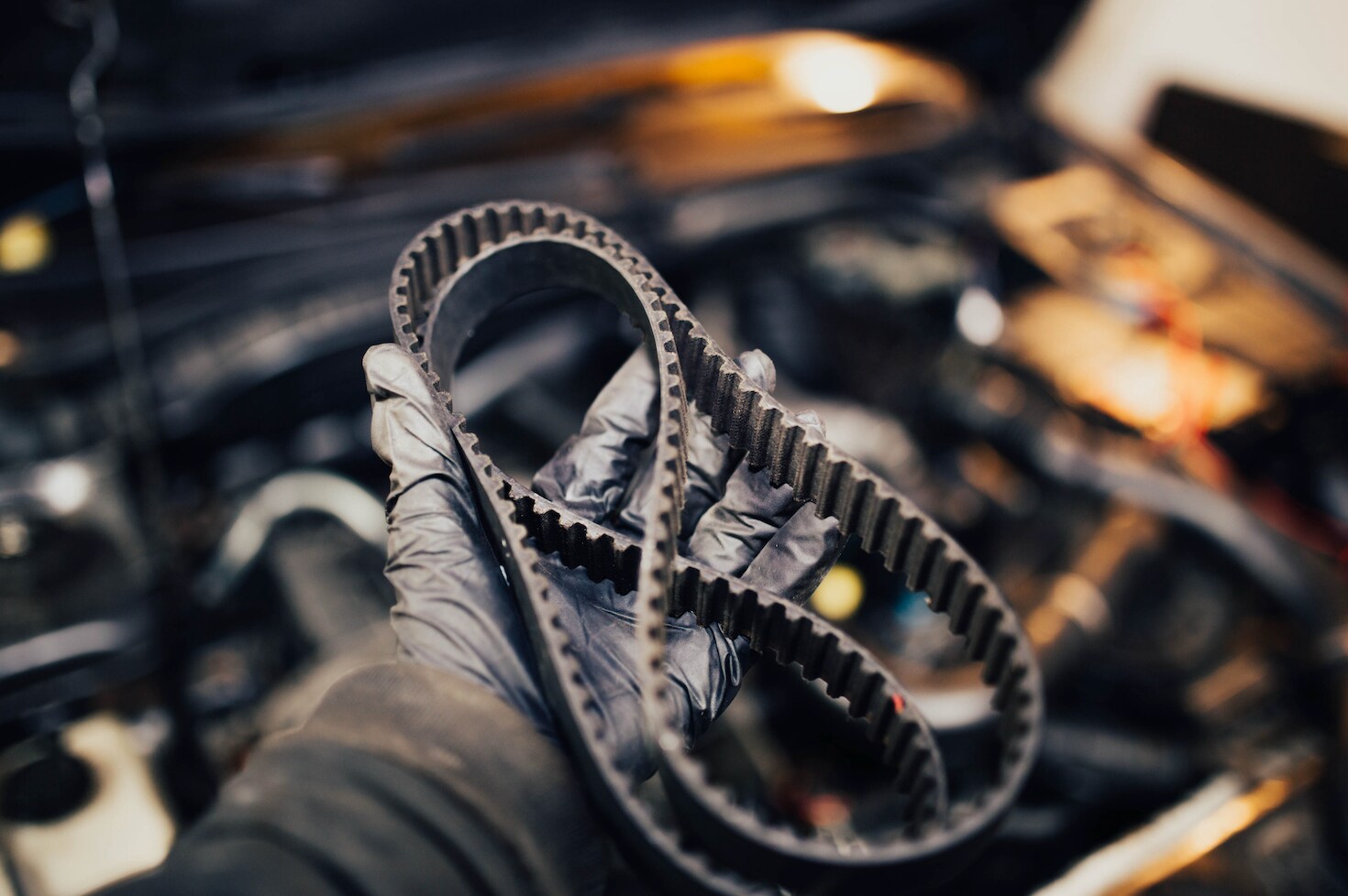 Mechanic with black gloves holding a timing belt.